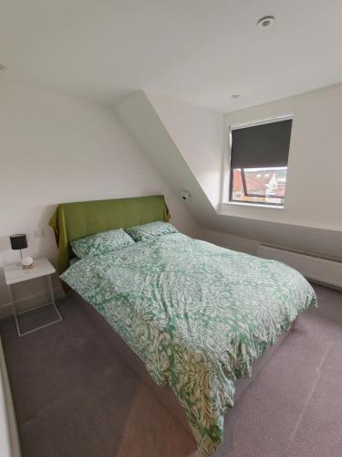 a bedroom with a bed with a green comforter and a window at Kilby close in Edgware