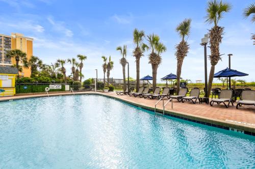 a swimming pool at a resort with chairs and palm trees at Monterey Bay Suites in Myrtle Beach