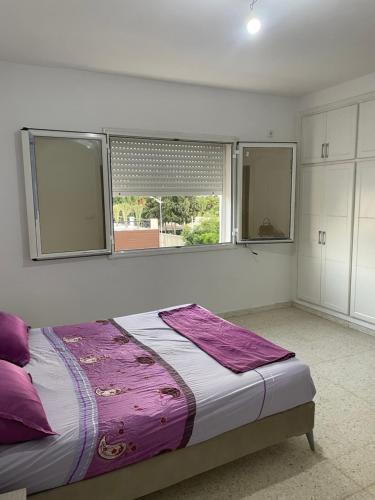 a bedroom with a bed with purple pillows and a window at Casa Cómoda in Nabeul