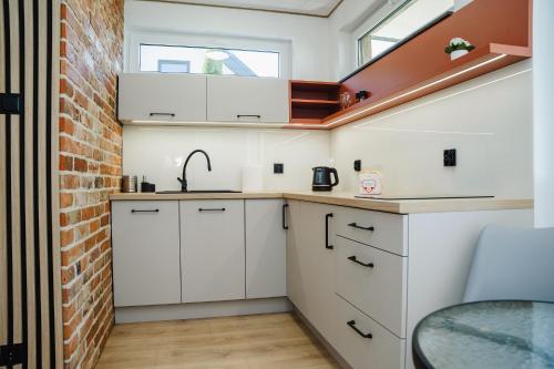 a kitchen with white cabinets and a brick wall at Morski Raj Apartamenty in Dębki