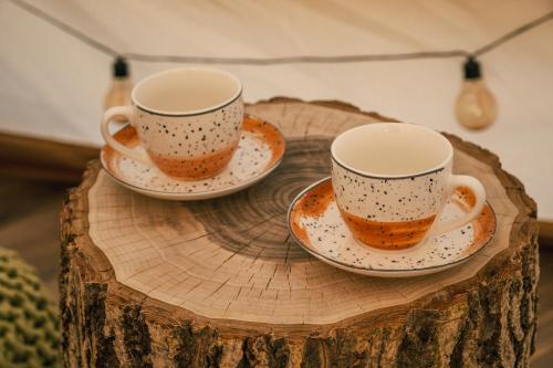 two cups and saucers sitting on a wooden stump at Zálesie Glamping in Kostolná Ves