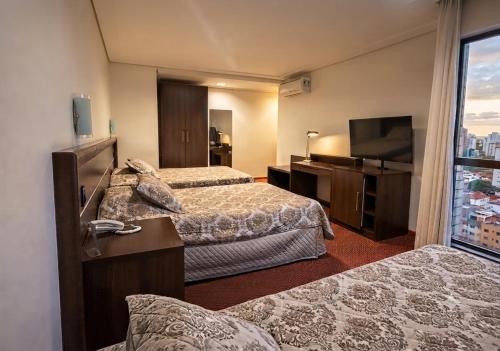a hotel room with two beds and a flat screen tv at Mogano Premium Hotel - ELETROPOSTO in Chapecó