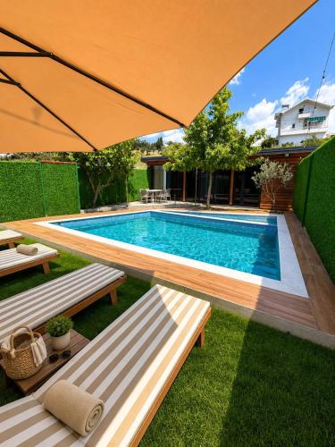 a swimming pool with two benches and an umbrella at Wooden Villa Eilin 3 in Tirana