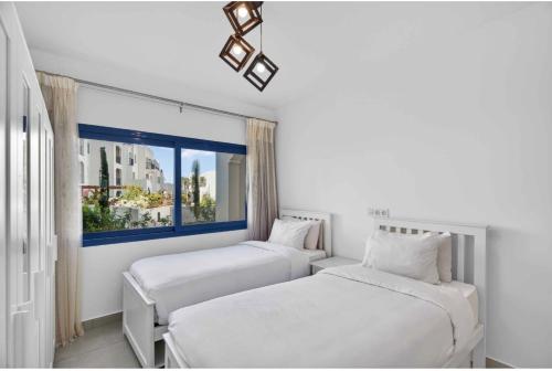 two beds in a white room with a window at Marassi in El Alamein