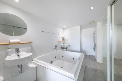 a white bathroom with a tub and a sink at Club Airlie in Airlie Beach