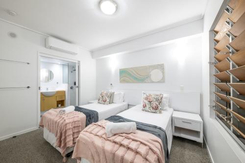 two beds in a white room with a sink at Club Airlie in Airlie Beach