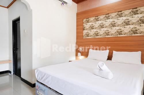 a bedroom with a white bed with a wooden headboard at As Waru Hotel RedPartner in Palang-Putih
