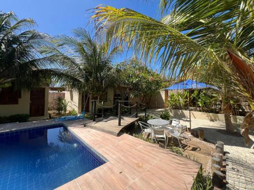a pool with a table and chairs and palm trees at Chalés Farol Village in Fortim