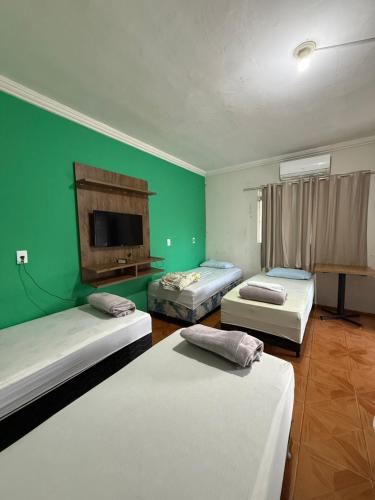 three beds in a room with a green wall at hotel paiol mutum in Nova Mutum