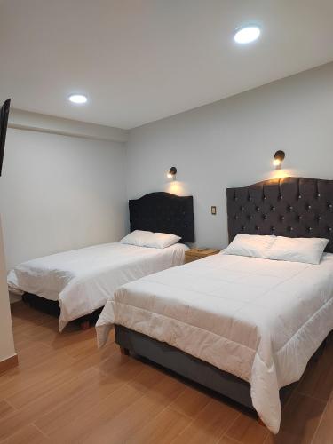 two beds in a room with white walls and wood floors at Pumaexplorer in Urubamba