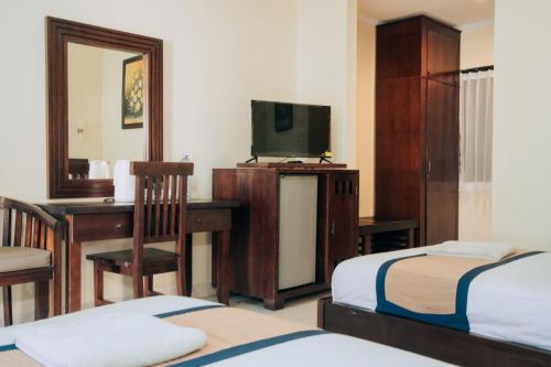 a hotel room with a desk and a tv and a bedroom at New Puri Asih Hotel in Kuta
