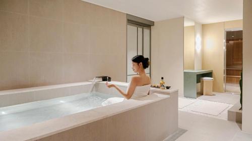a woman sitting in a bath tub in a bathroom at Anook Hotel Busan Gwangalli in Busan