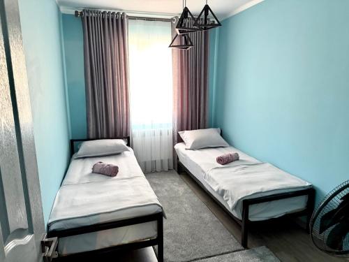 two beds in a room with blue walls and a window at Joy Fergana Guesthouse in Fergana