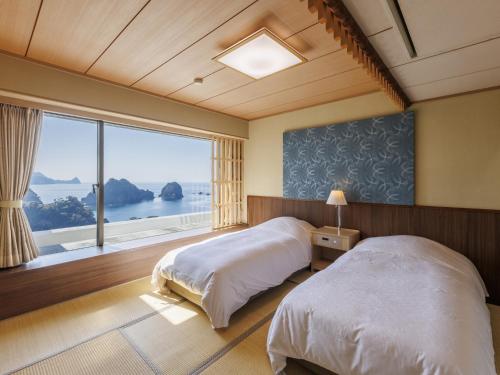 a bedroom with two beds and a large window at Dogashima New Ginsui in Nishiizu