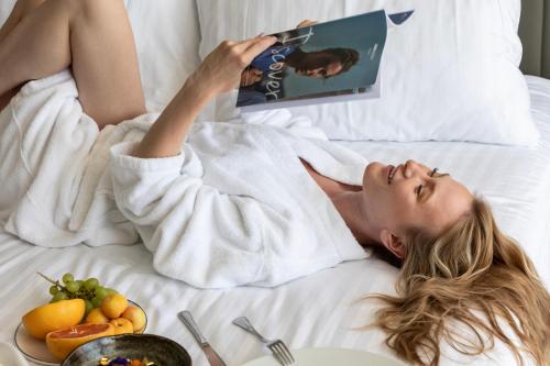 a woman laying in bed with a book and a plate of fruit at Royal Apollonia by Louis Hotels in Limassol
