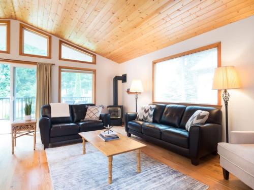 a living room with black leather furniture and wood ceilings at Woodland Bungalow in Glacier