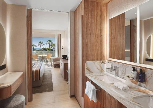 a bathroom with a sink and a room with a bed at Olympic Lagoon Resort Paphos in Paphos
