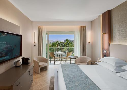 a hotel room with a bed and a television and a table at Olympic Lagoon Resort Paphos in Paphos