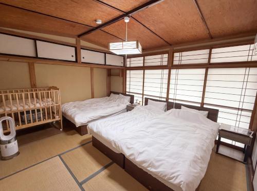 ein Schlafzimmer mit zwei Betten, einem Kinderbett und Fenstern in der Unterkunft かんさんのお宿 in Fuji