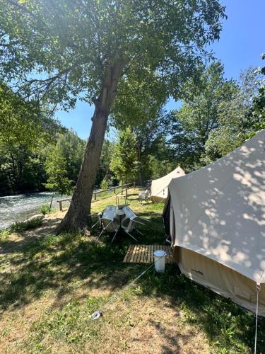 a tent under a tree next to a river at Camping Noguera Pallaresa in Sort