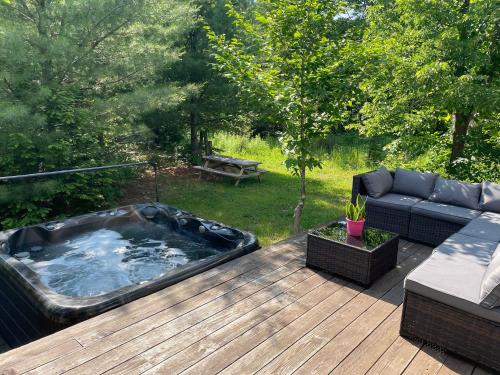 a hot tub on a wooden deck with a couch at Spa et Waterfront - Cachette du Petit Lac in Chertsey