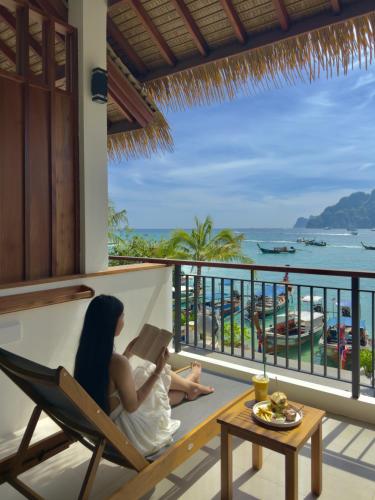 Eine Frau sitzt auf einem Stuhl auf einem Balkon und liest ein Buch. in der Unterkunft Phi Phi at Pier in Ko Phi Phi