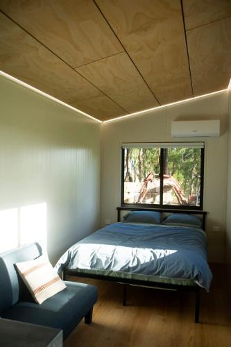 a bedroom with a bed and a window and a couch at The Lorikeet Tiny Home with Stunning Views in Canoelands