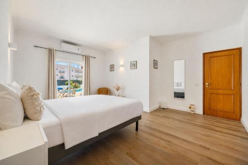 a white bedroom with a large bed and a wooden door at Luz Sun Poolhouse in Luz