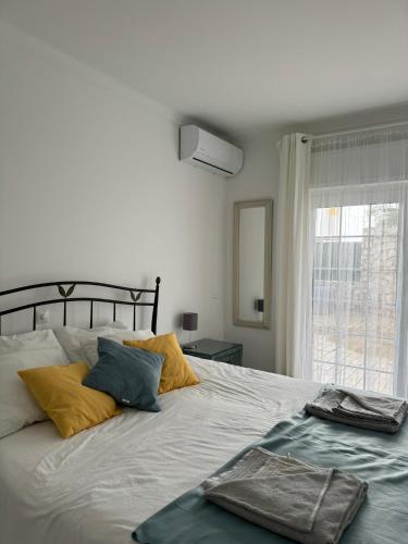 a white bed with yellow and blue pillows and a window at Seabreeze T3 in Carvoeiro