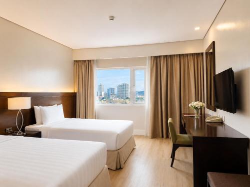 a hotel room with two beds and a desk and a window at Harolds Hotel Cebu in Cebu City