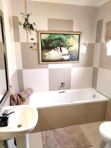 a bathroom with a tub and a sink and a painting on the wall at Riverside Cottages in Graaff-Reinet