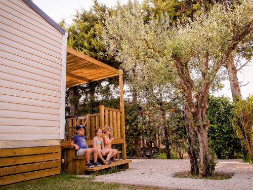 a boy and two girls sitting on a wooden play house at Camping Pegomas in Saint-Rémy-de-Provence
