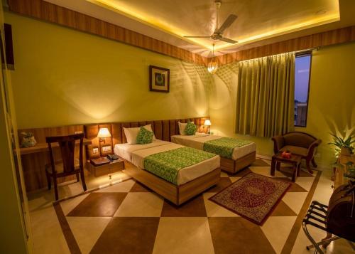 a bedroom with two beds and a chair and a window at Hotel Gems Suites in Jaipur