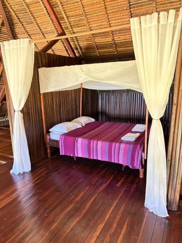 ein Bett in einem Zimmer mit Vorhängen und Holzboden in der Unterkunft Villa TiPunch in Nosy Be