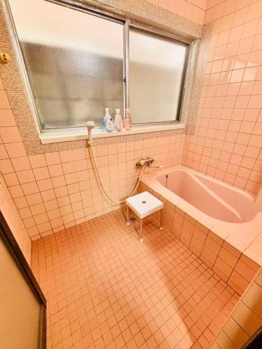 a pink tiled bathroom with a tub and a window at 古民家一棟貸切 民宿 潤 松山市駅徒歩5分 銀天街徒歩2分 無料駐車場1台付き in Matsuyama