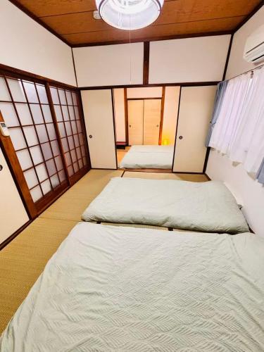 two beds in a small room with windows at 古民家一棟貸切 民宿 潤 松山市駅徒歩5分 銀天街徒歩2分 無料駐車場1台付き in Matsuyama