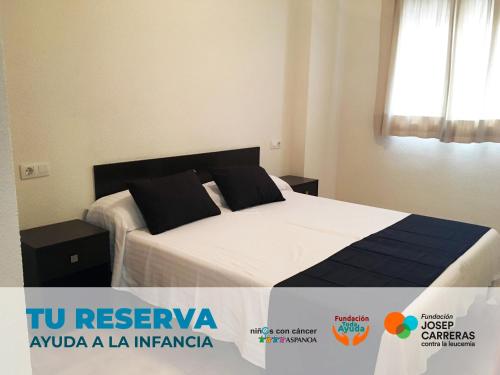 a bedroom with a bed with white sheets and black pillows at Apartamentos Doña Carmen 3000 in Oropesa del Mar