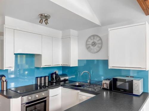 a kitchen with white cabinets and a clock on the wall at Sunset in St Austell