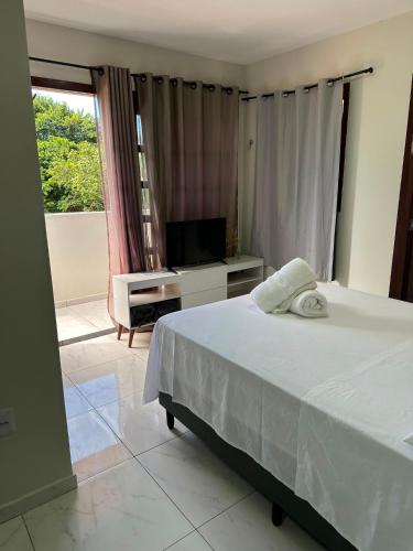 a bedroom with a white bed and a television at Casa Flora & Mar in Pipa