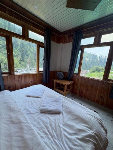 a bedroom with a large white bed with windows at Gaunnie Valley - Jibhi in Jibhi