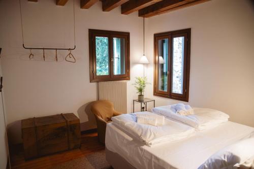 a bedroom with a bed and a chair and two windows at Locanda Hemingway in Bassano del Grappa