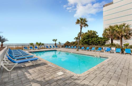 a swimming pool with blue lounge chairs and the ocean at Captain's Quarters Resort in Myrtle Beach