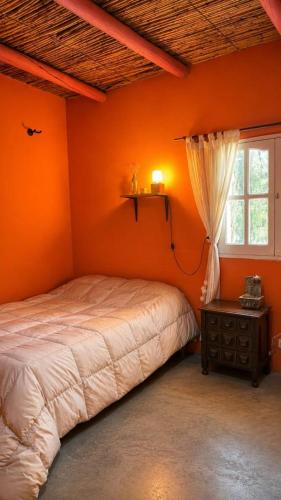 a bedroom with an orange wall with a bed and a window at Tale Cabaña de campo in Huacalera
