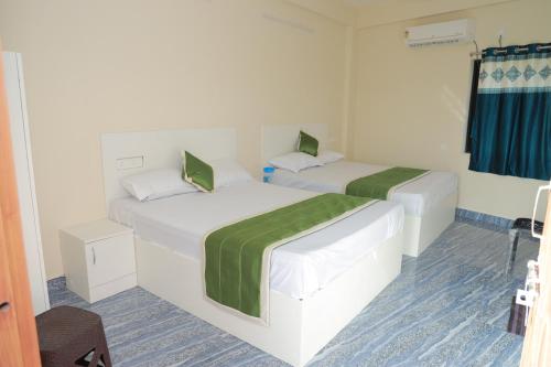 two beds in a white room with green sheets at Vetri Residency in Agastīswaram