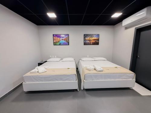 two beds in a white room with paintings on the wall at Palhoça Hotel in Canindé