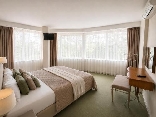 a bedroom with a bed and a desk and windows at Apartamentai Palangoje Arune in Palanga
