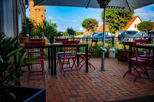 ein Tisch mit roten Stühlen und einem Sonnenschirm auf einer Terrasse in der Unterkunft Restaurant und Pension Zur Wildgans in Arendsee