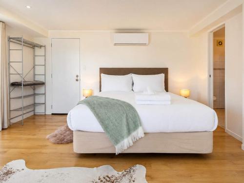 a bedroom with a large white bed with a green blanket at Aqua Sands #1 - Stay Waiheke in Oneroa