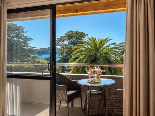 a balcony with a table and chairs and a large window at Aqua Sands #2 - Stay Waiheke in Oneroa