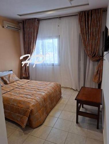 a bedroom with a bed and a table and a window at Hôtel Les Pyramides in Yaoundé